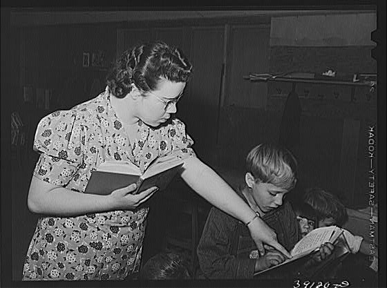 Image of a mid-twentieth-century schoolteacher pointing at a page in a pupil's book