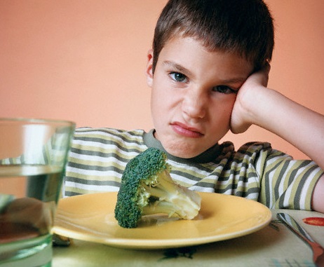 Child makes grumpy face behind plate of broccoli