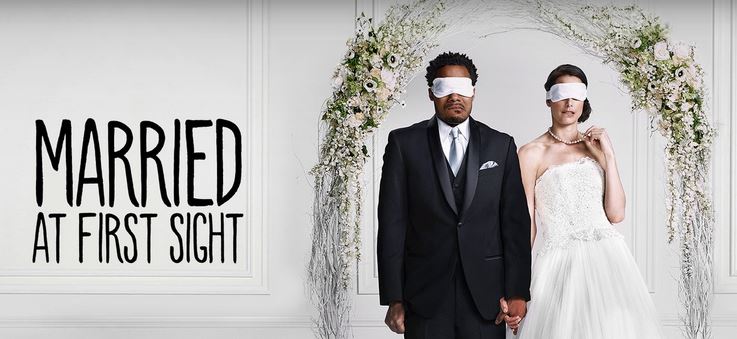 A man and a woman wearing blindfolds and holding hands next to the words "Married at First Sight"