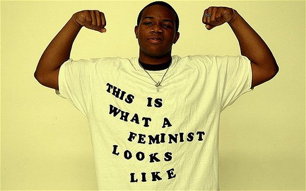 Young Black man flexes biceps while wearing shirt that reads, "This is what a feminist looks like"
