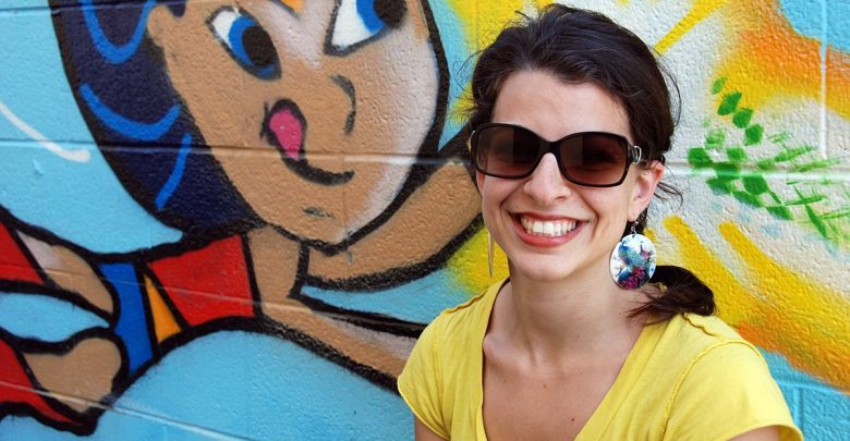 Anita Sarkeesian smiling, in front of a wall with Wonder Woman graffiti art