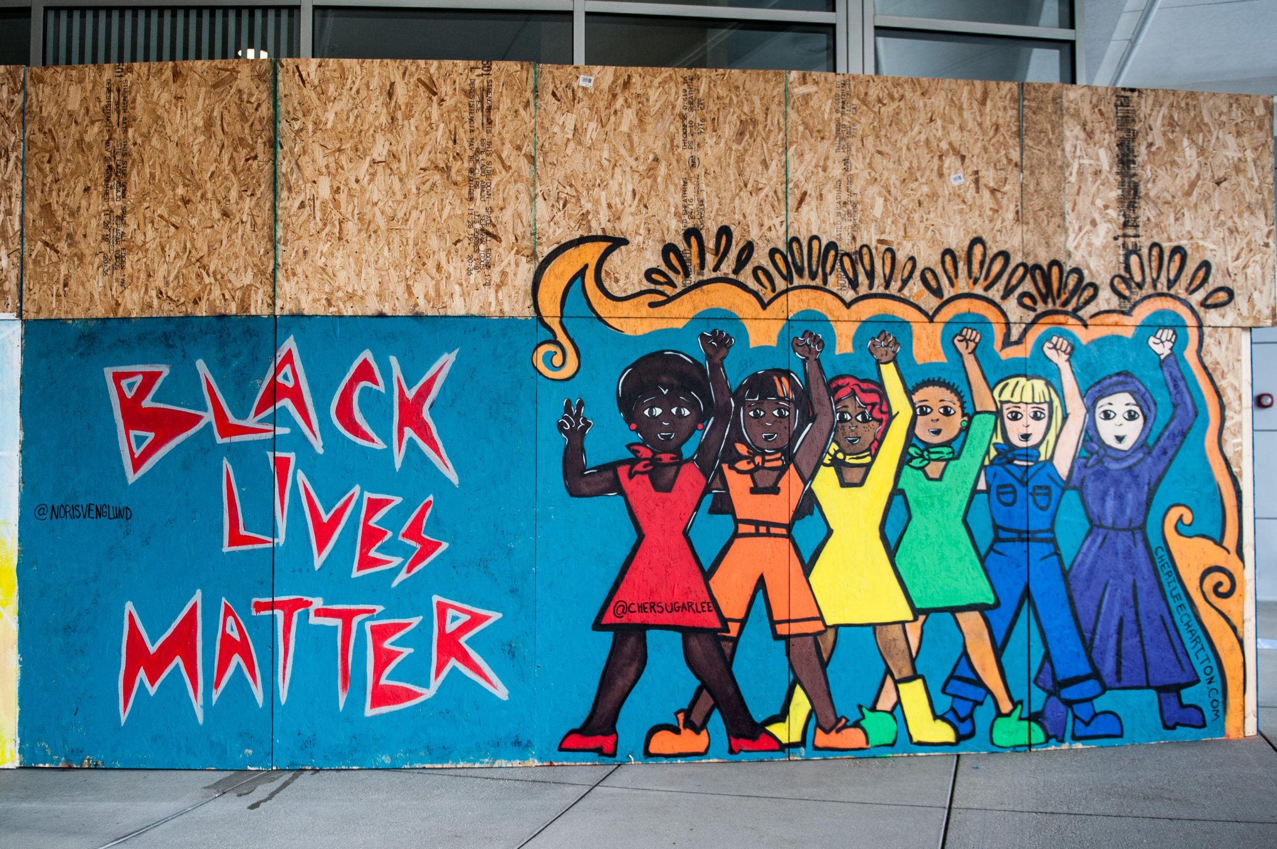Two board murals. The left one says "Black Lives Matter" and the right one features women of different ethnicities all holding their fists up in solidarity.
