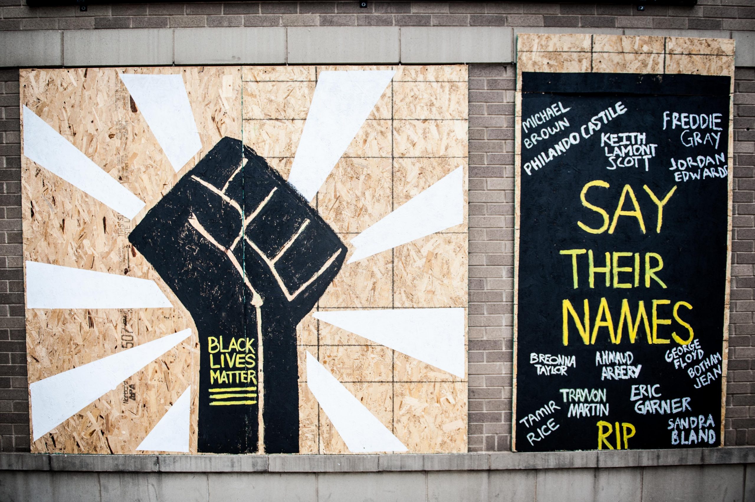 Two board murals. The left one features a solidarity fist with the words "Black Lives Matter." On the right is says "Say Their Names" and lists the names of many of the black victims of police violence.